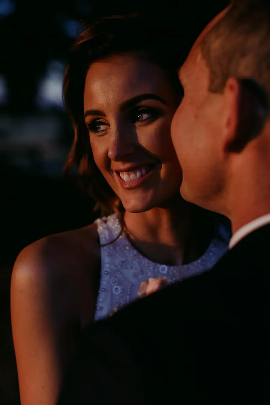 Close portrait of a smiling bride beside the groom in dim light.