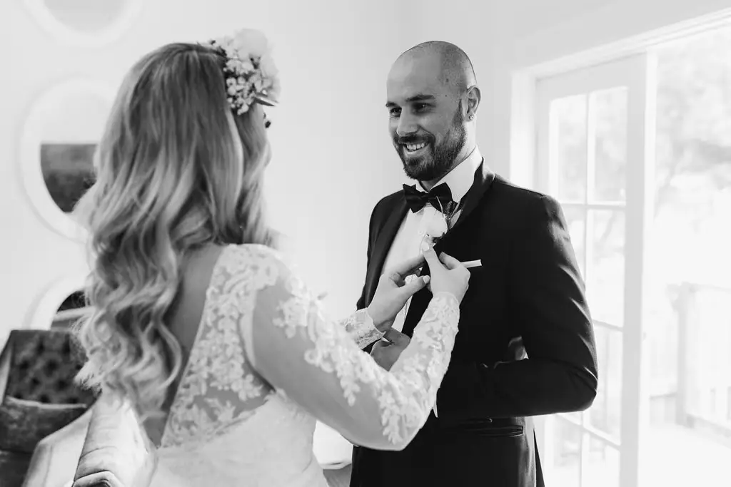 Black-and-white photograph of the bride adjusting the groom's bow tie.