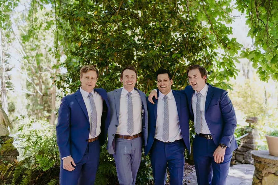 Groom and three groomsmen smiling together beneath garden greenery