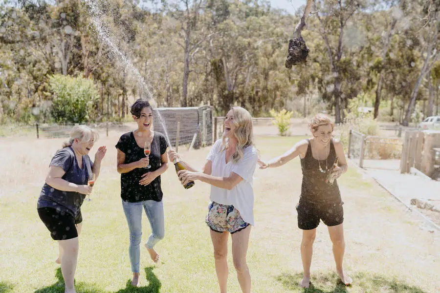 Women stepping back and laughing while sparkling wine sprays outdoors