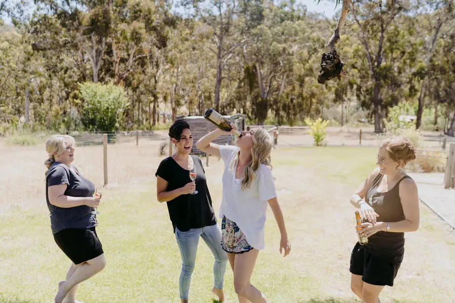 Woman drinking from a bottle while friends stand beside her on a lawn