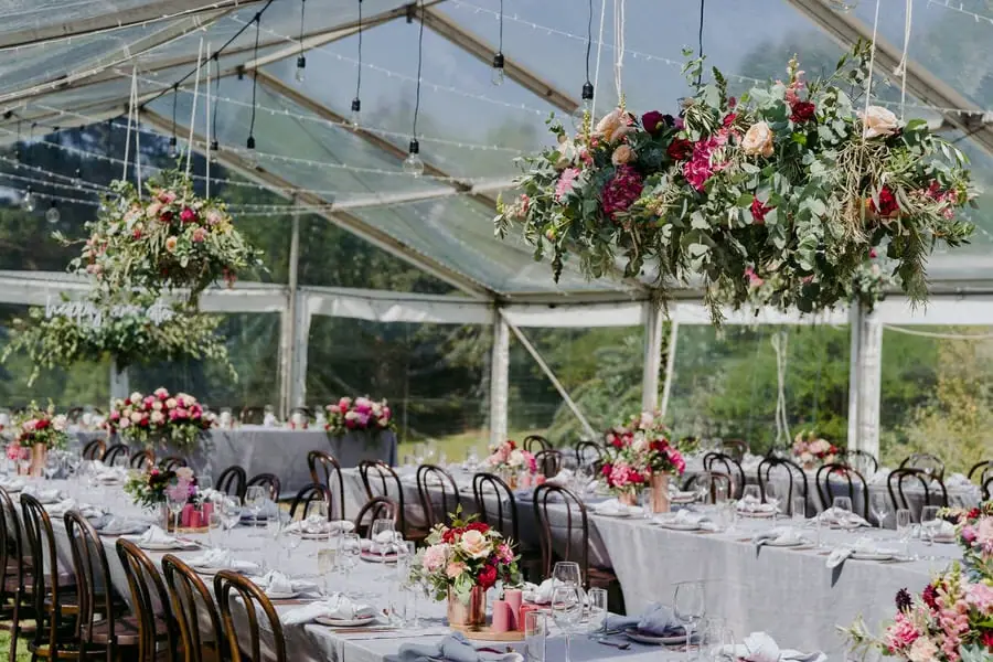Reception tables beneath hanging flower arrangements in a clear-roofed marquee