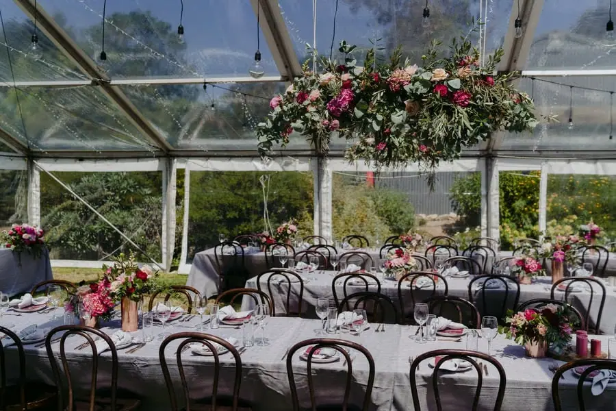 Round reception tables set with flowers and black chairs inside a clear marquee