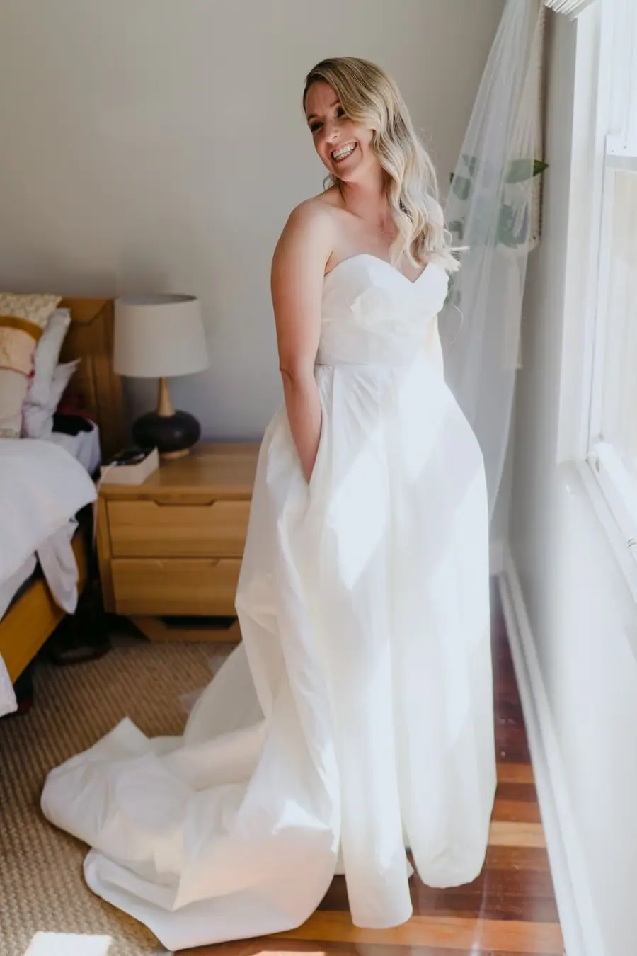 Bride standing beside a window with her dress train on the floor