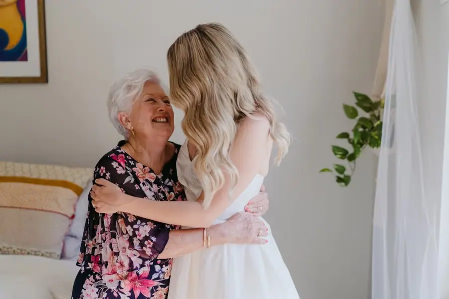 Bride embracing a smiling grey-haired woman in a floral dress