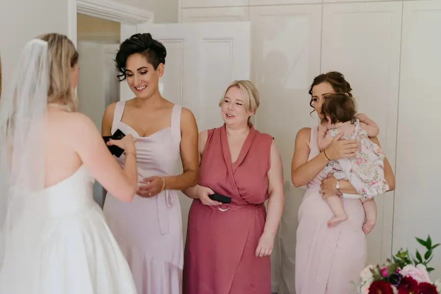 Bride facing bridesmaids indoors with one holding a baby