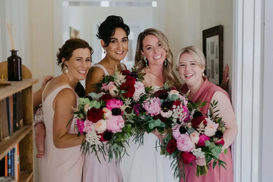 Bride and bridesmaids smiling together with colourful bouquets indoors