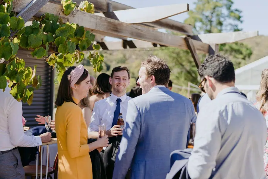 Guests chatting with drinks beneath a vine-covered veranda