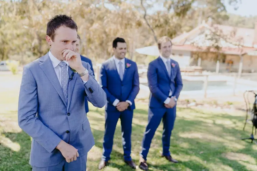 Groom wiping his eye as groomsmen wait behind him at the ceremony