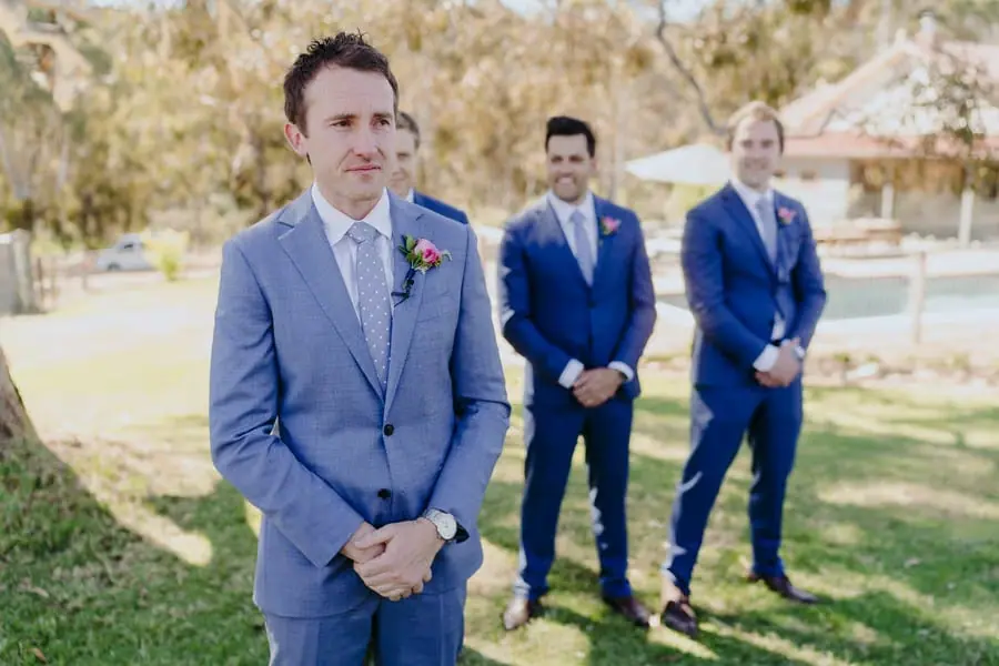 Groom waiting with his hands clasped before the outdoor ceremony