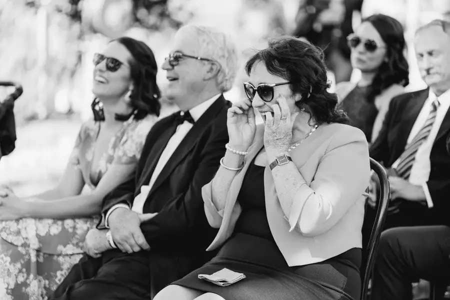 Black and white photograph of guests smiling and holding their hands near their faces