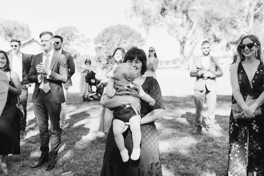 Black and white photograph of standing guests with a woman holding a baby