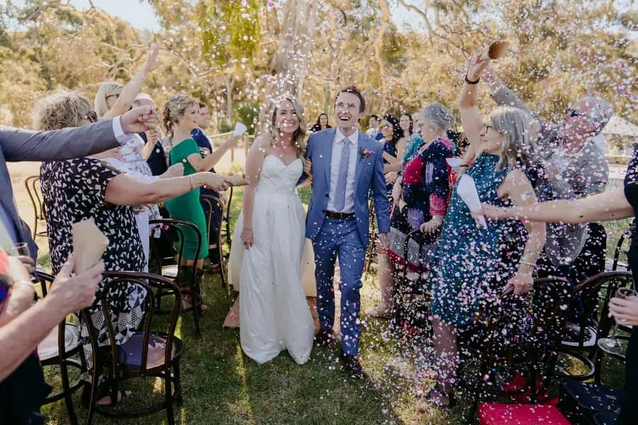 Couple walking through colourful confetti thrown by cheering wedding guests