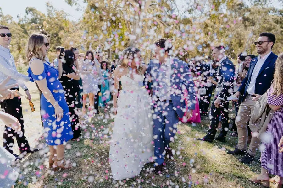 Bride and groom smiling as colourful confetti fills the aisle