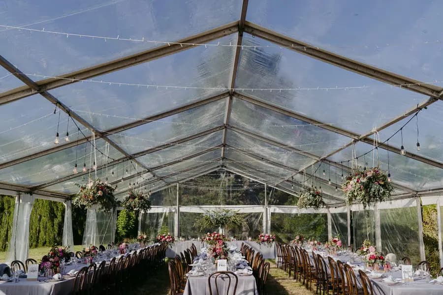Wide view of long reception tables and hanging flowers beneath a clear marquee roof