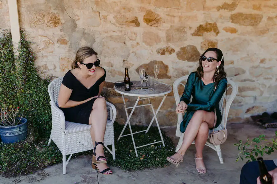 Two guests in sunglasses laughing while seated beside a stone wall
