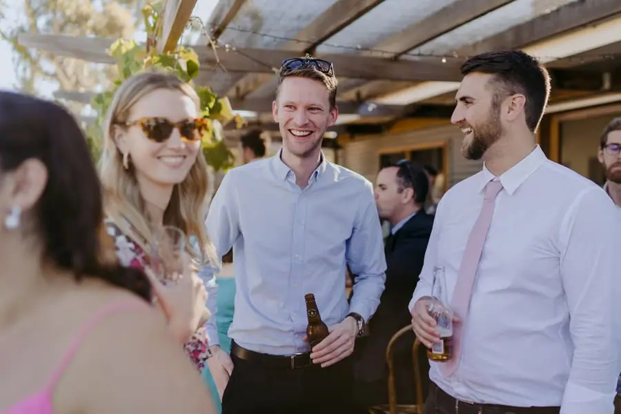 Guests smiling together with drinks beneath a vine-covered veranda
