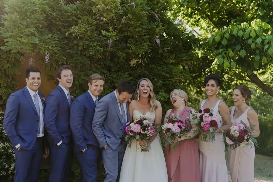 Wedding party laughing together beneath leafy trees