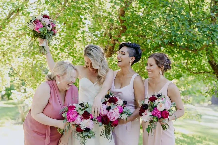 Bride raising her bouquet while laughing with bridesmaids