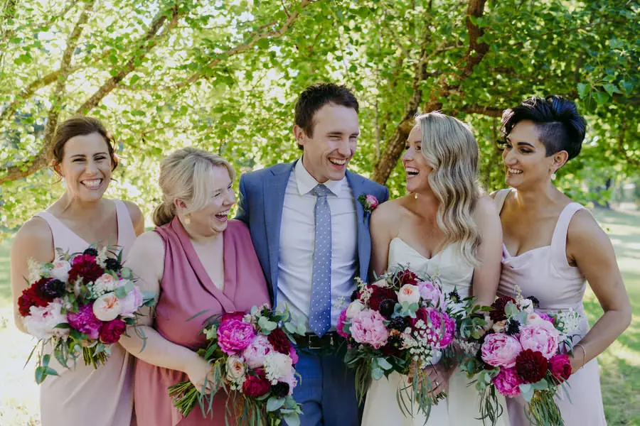 Groom laughing beside the bride and bridesmaids with their bouquets