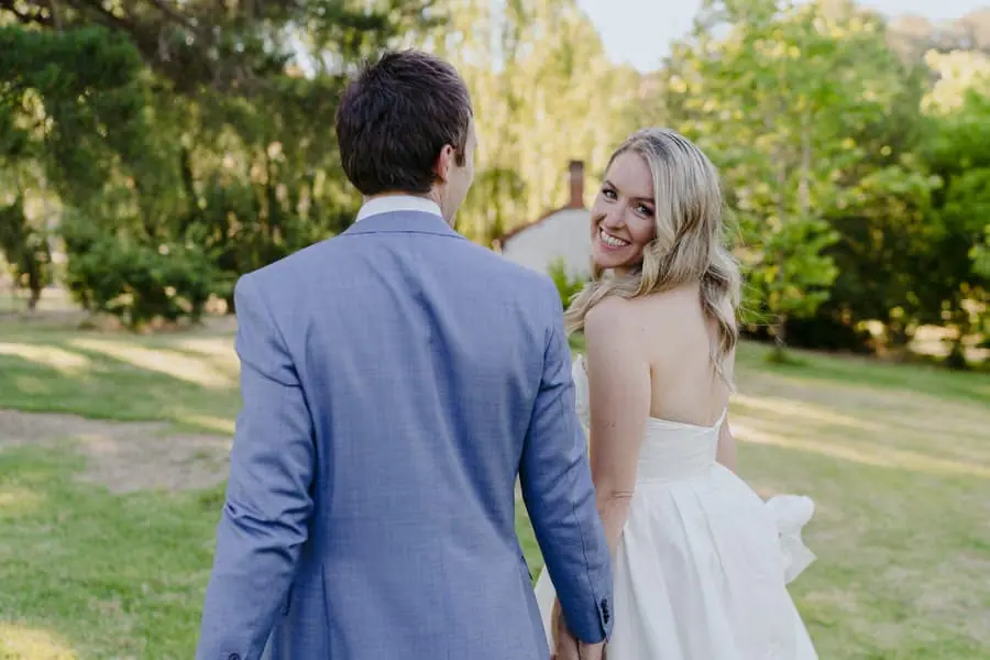 Bride smiling back toward the groom while they hold hands in the garden