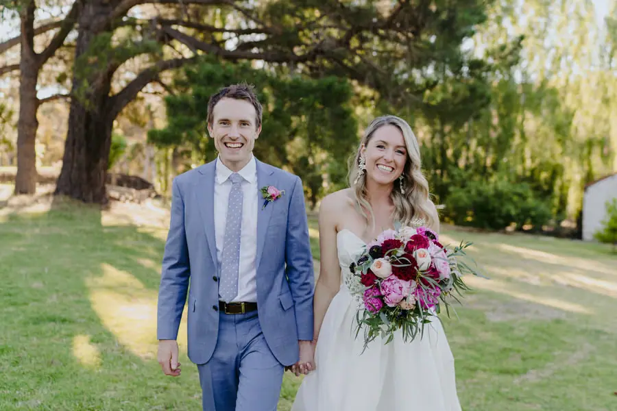 Bride and groom smiling toward the camera on a garden lawn