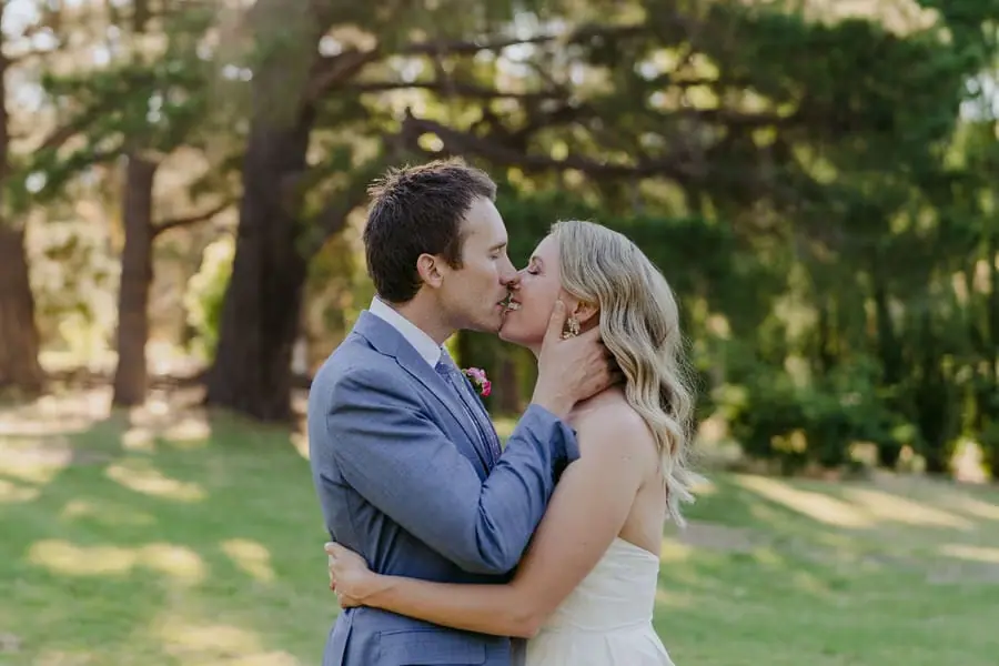 Bride and groom kissing beneath leafy trees