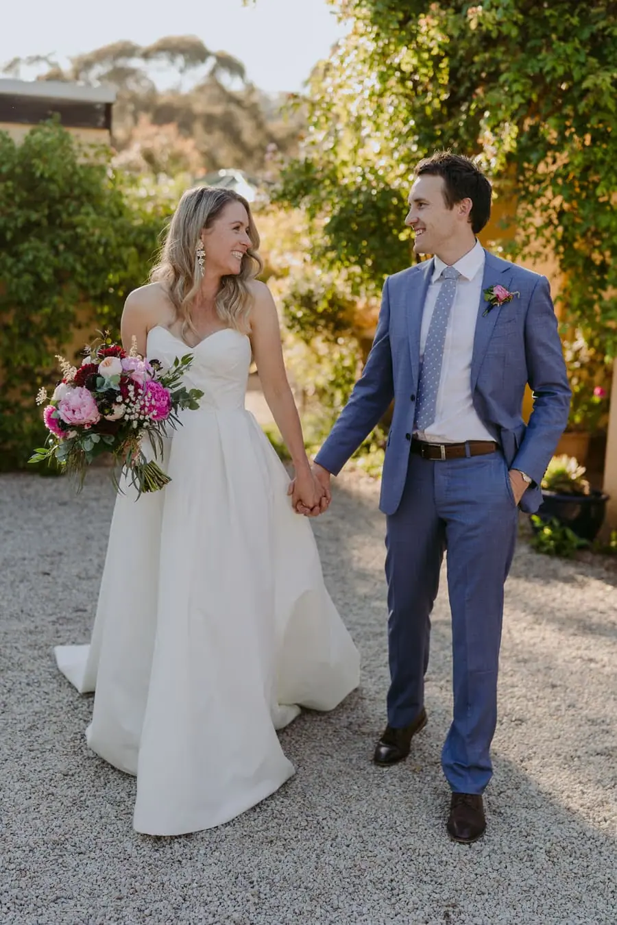 Bride and groom holding hands while walking along a garden path