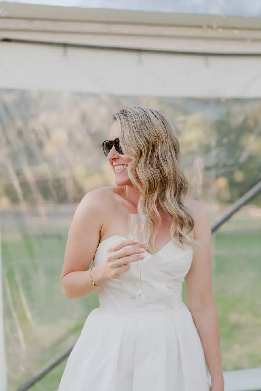 Bride smiling in sunglasses while standing inside the reception marquee