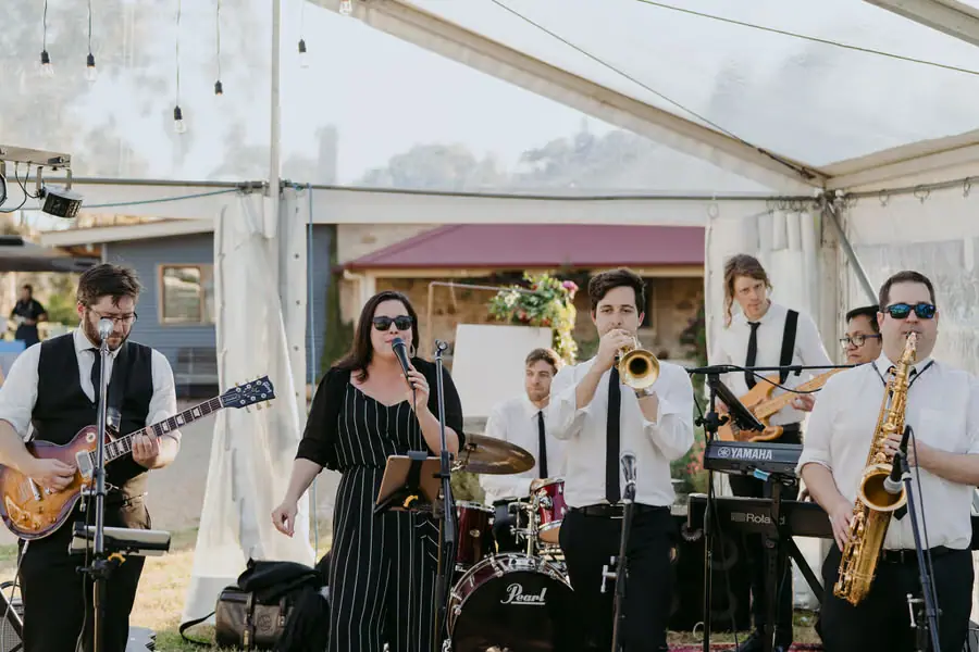 Band performing with guitar, vocals, trumpet and saxophone inside the marquee