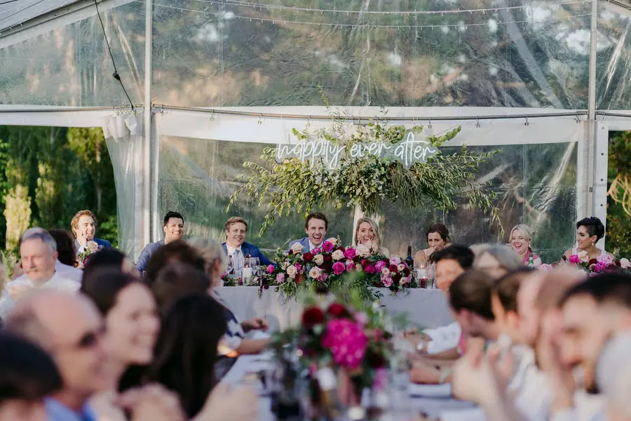 Guests smiling across flower-decorated tables inside the marquee