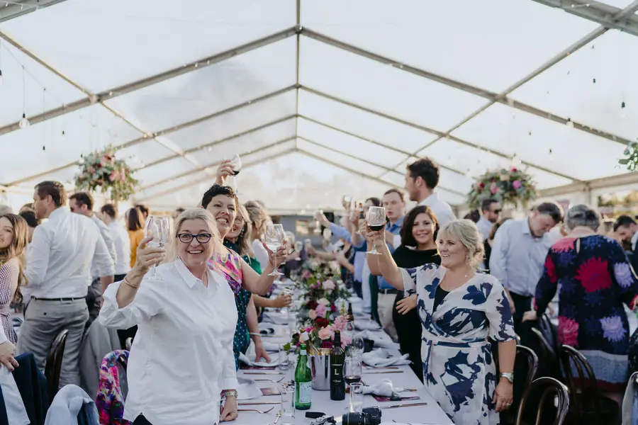 Wedding guests raising their glasses in a toast beneath the marquee roof