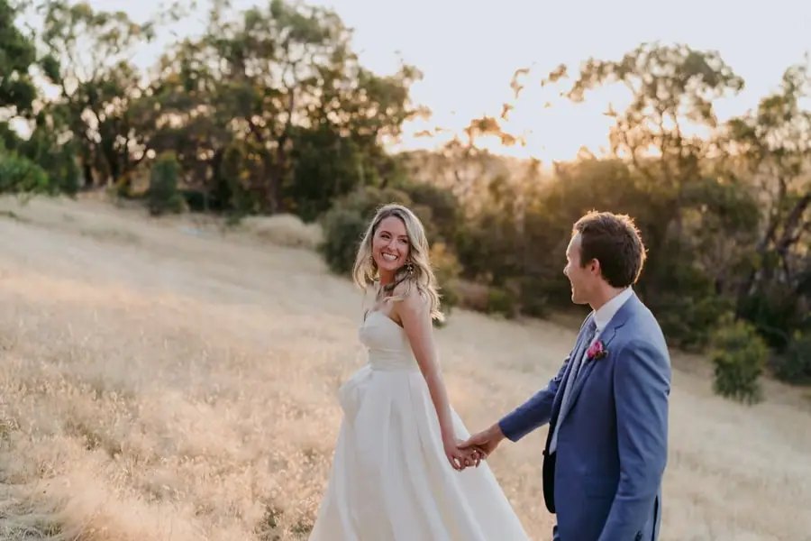 Bride smiling back at the groom as they hold hands in a field