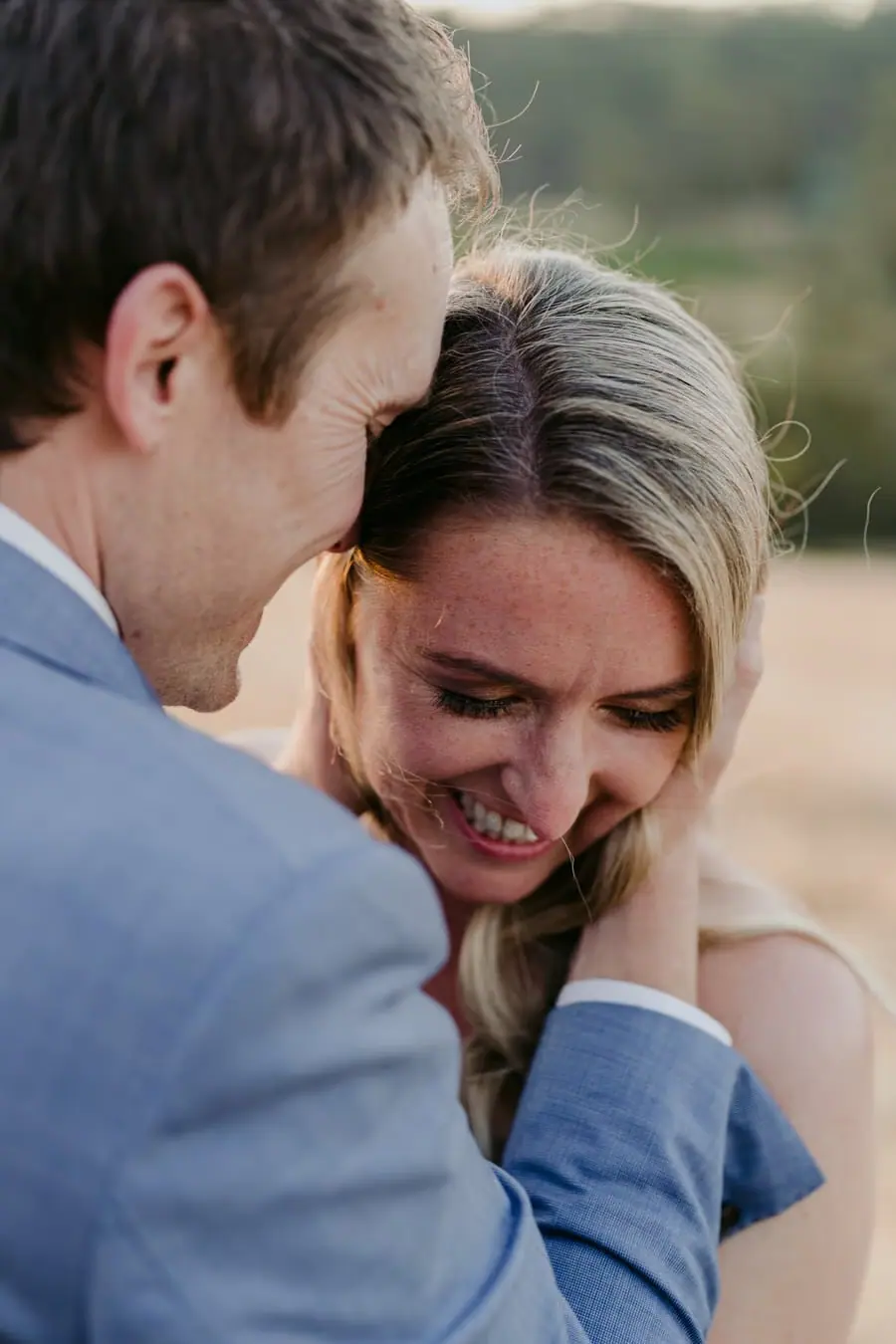 Bride laughing while leaning against the groom in a sunlit field
