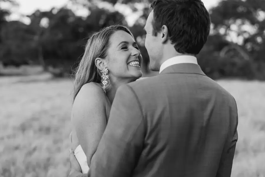 Black and white photograph of the bride laughing as the groom embraces her