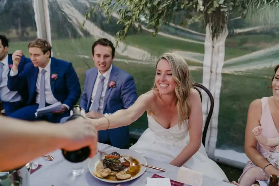 Bride smiling and raising a glass toward a guest at the reception table
