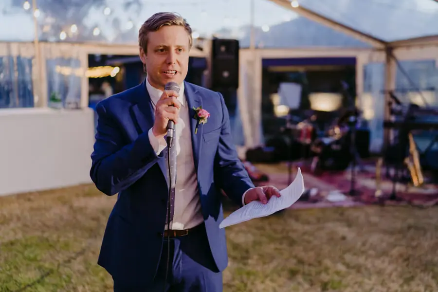 Groomsman speaking into a microphone while holding speech notes