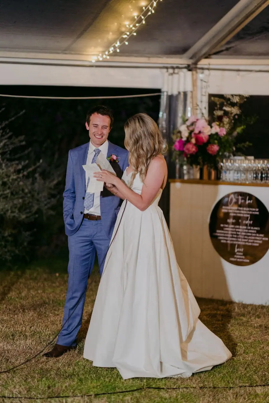 Bride and groom holding a microphone together beside the reception marquee
