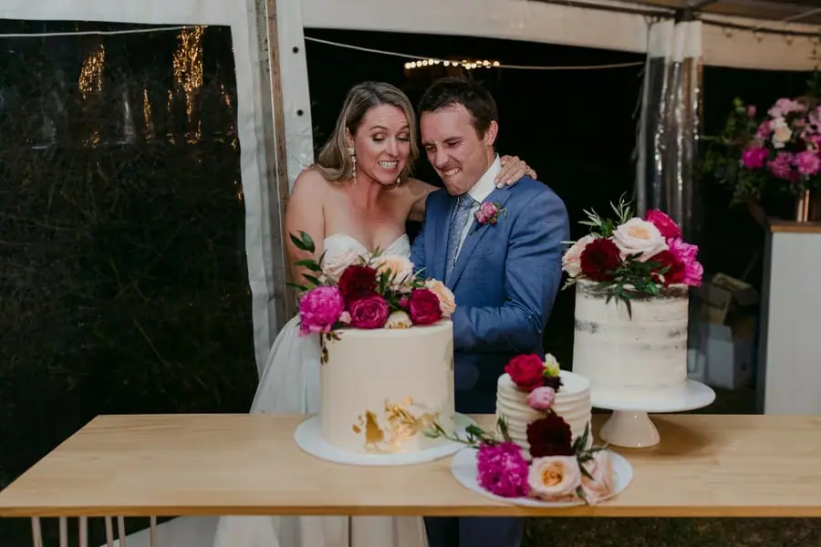 Bride and groom cutting a flower-decorated wedding cake beside another white cake