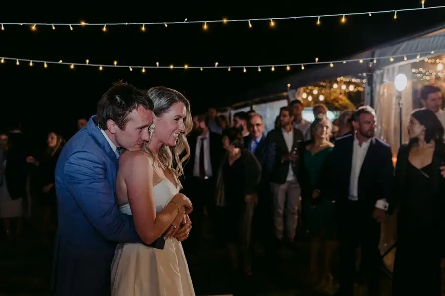 Groom embracing the bride from behind as guests watch their dance