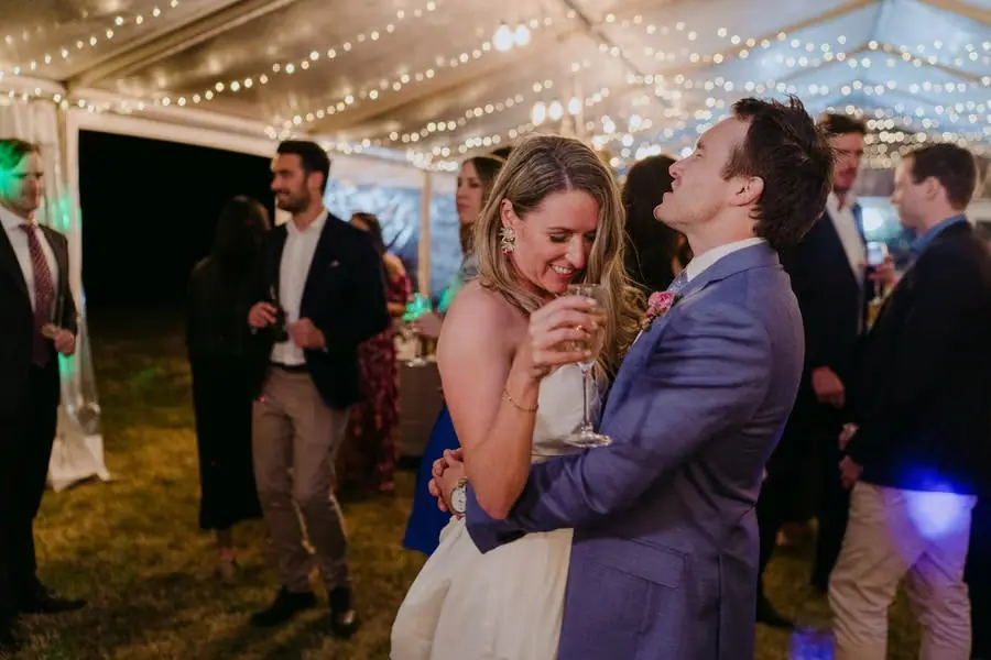 Bride and groom laughing closely together beneath reception fairy lights