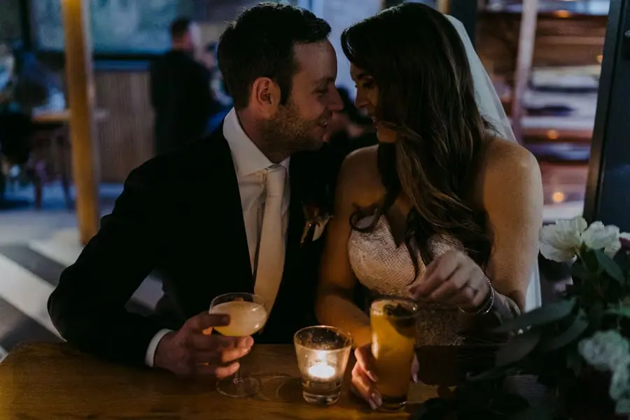 Couple sits close together holding drinks beside a candle.