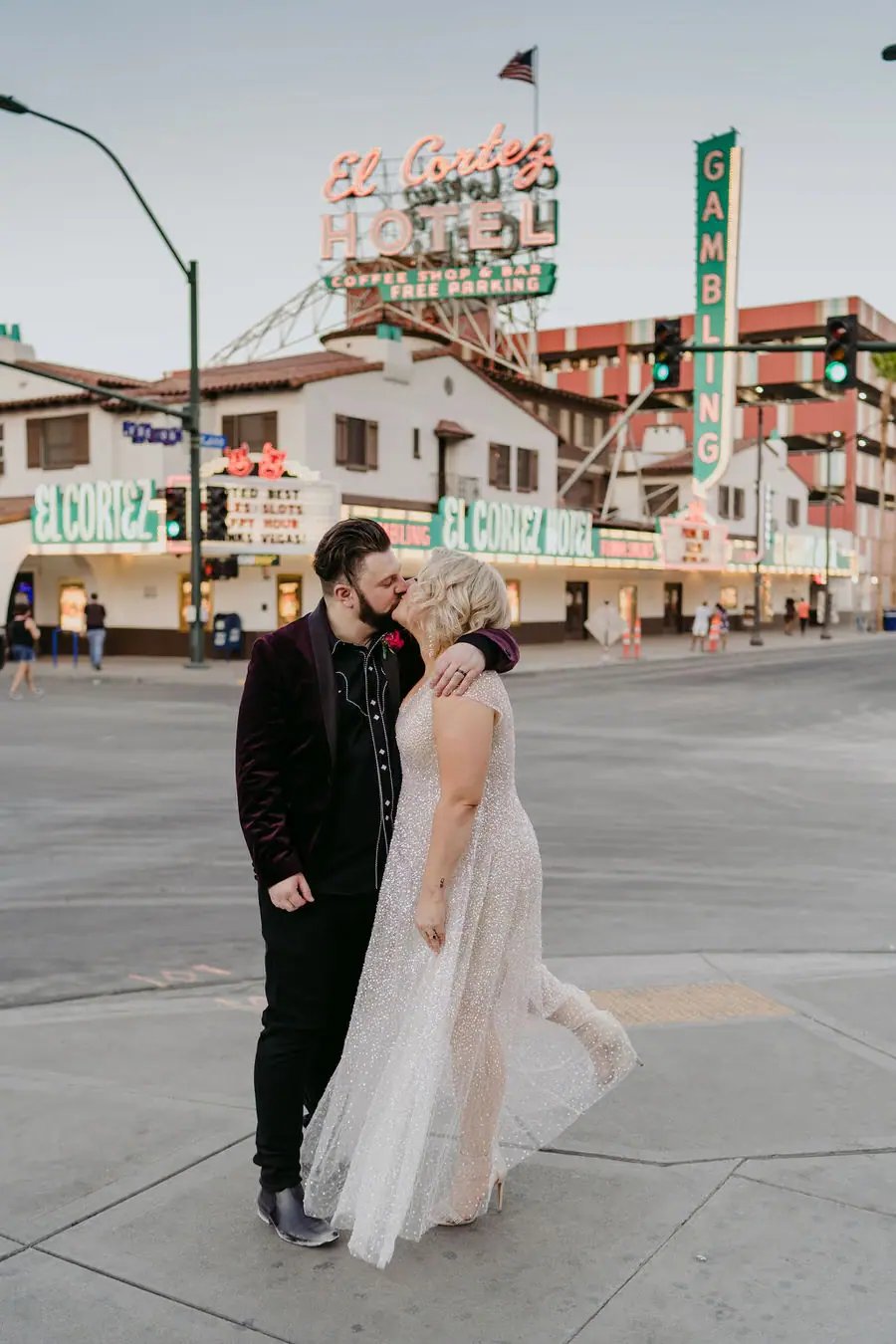 Couple kisses on a city pavement with colourful signs behind them.