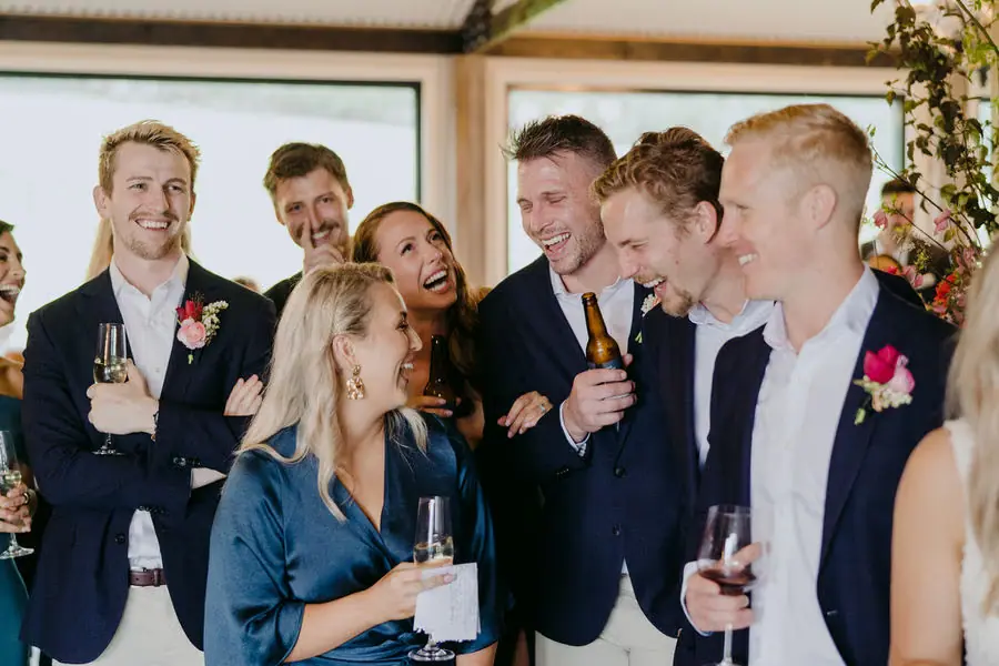 Guests laugh together holding drinks indoors.