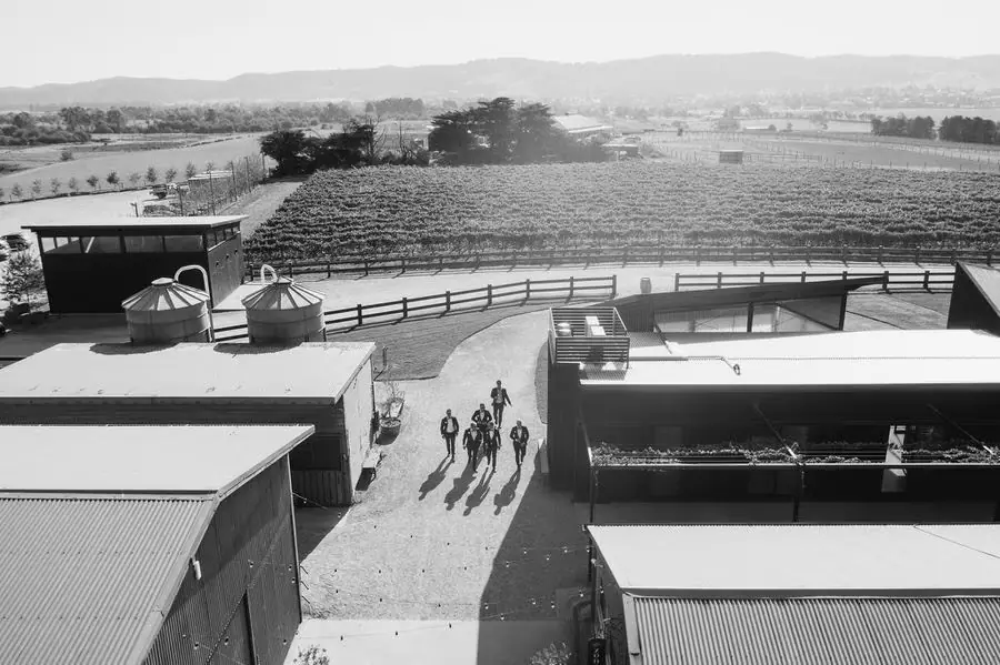 Black and white aerial view of people walking between venue buildings with vineyards beyond.