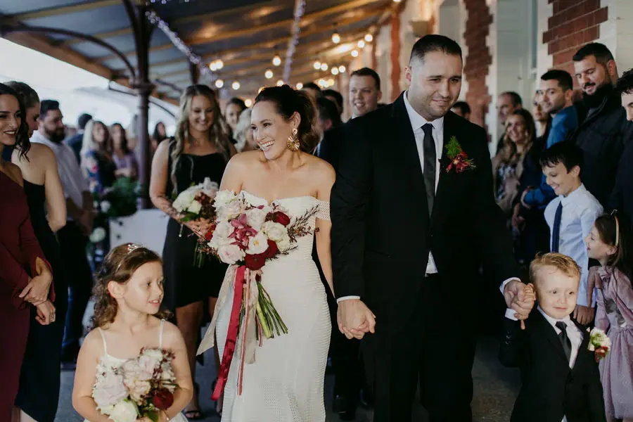 Newlyweds walk through guests with children beside them.