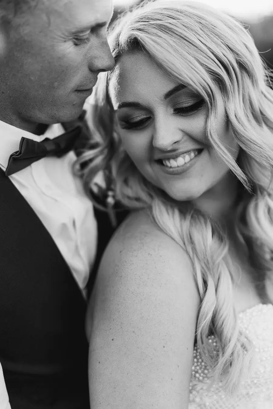 Black and white portrait of the groom kissing the smiling bride's forehead.