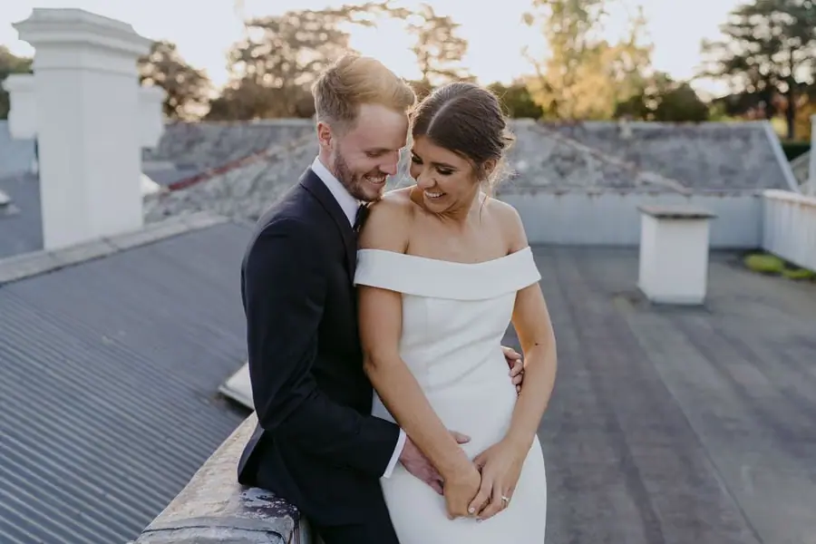 Groom embraces the bride from behind on a rooftop.