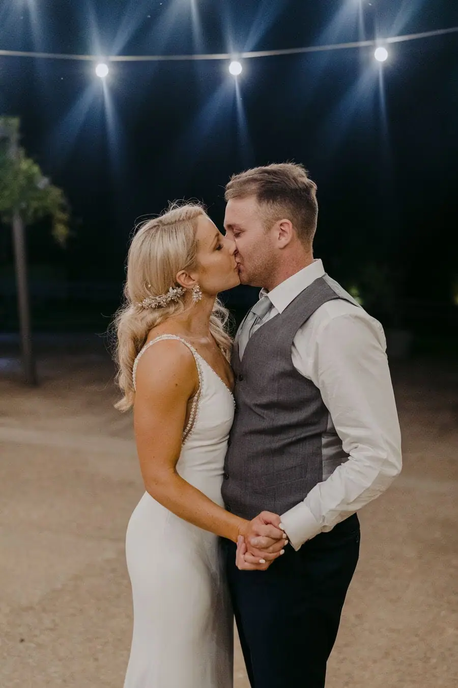 Couple kisses beneath outdoor lights at night.