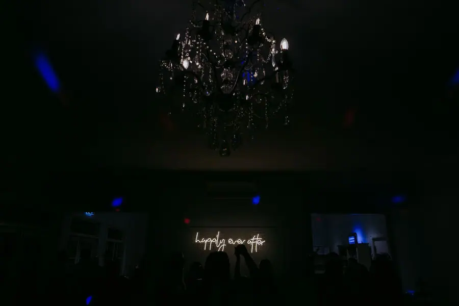 Chandelier and glowing wedding sign in a dark reception room.
